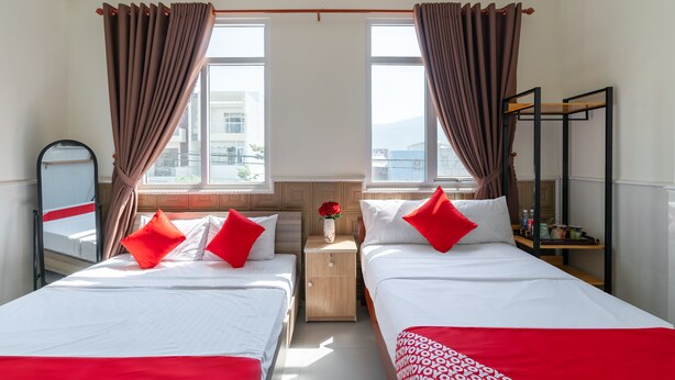 A hotel room with two beds, a nightstand with a vase of flowers, and a shelf with kitchen items. - OYO 238 Luxury Motel (Da Nang)