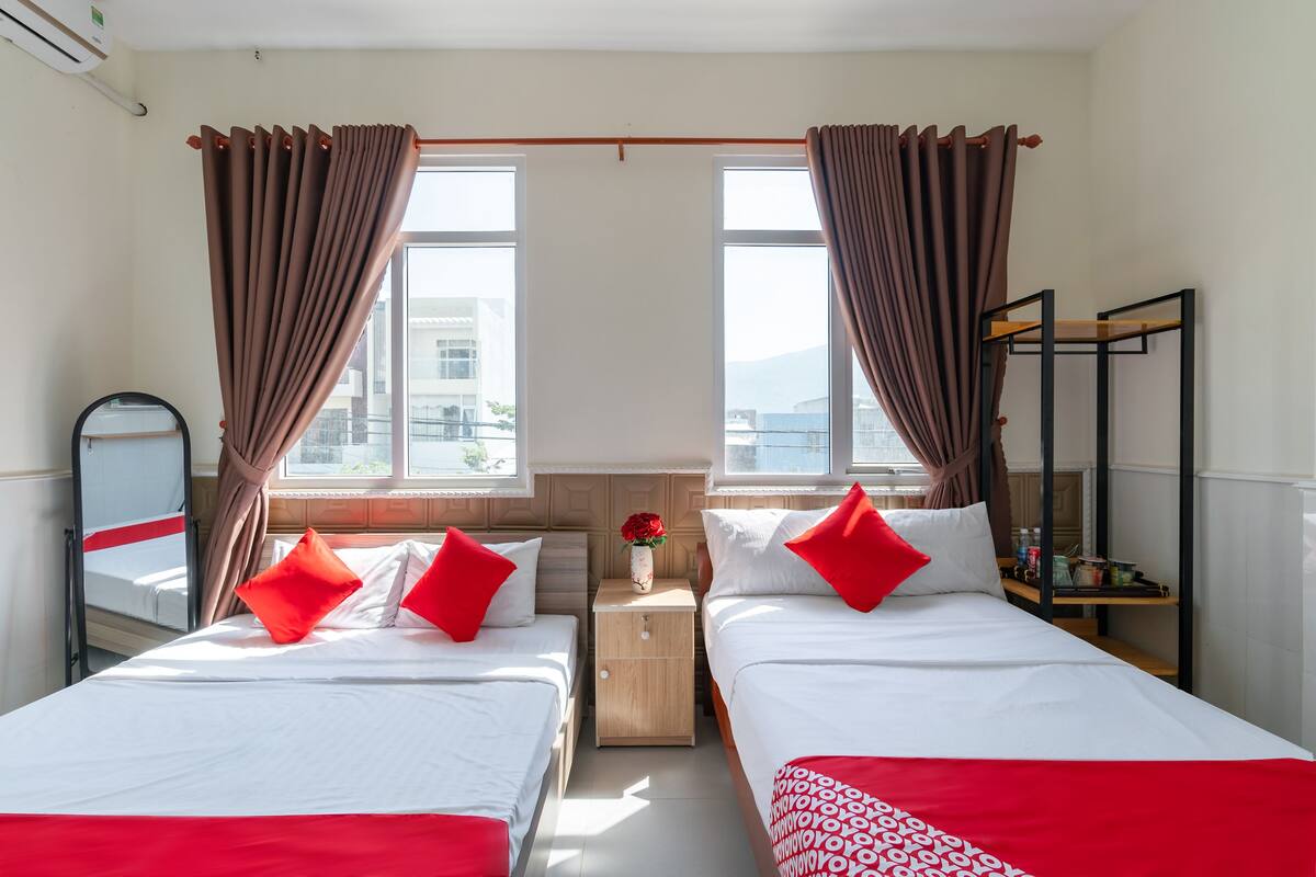 Une chambre d’hôtel avec deux lits, une table de chevet ornée d’un vase de fleurs et une étagère contenant des ustensiles de cuisine.
