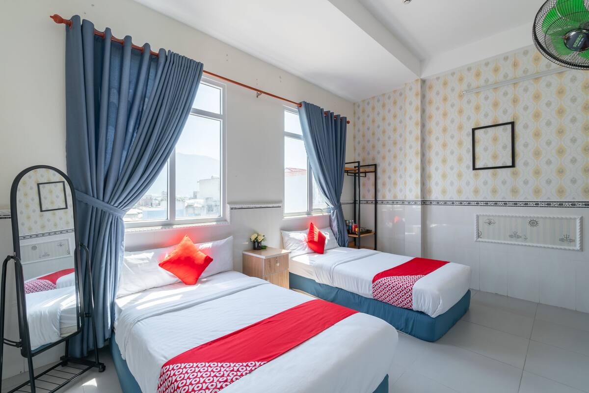 Une chambre d’hôtel avec deux lits, une table de chevet, un miroir et une fenêtre avec des rideaux.