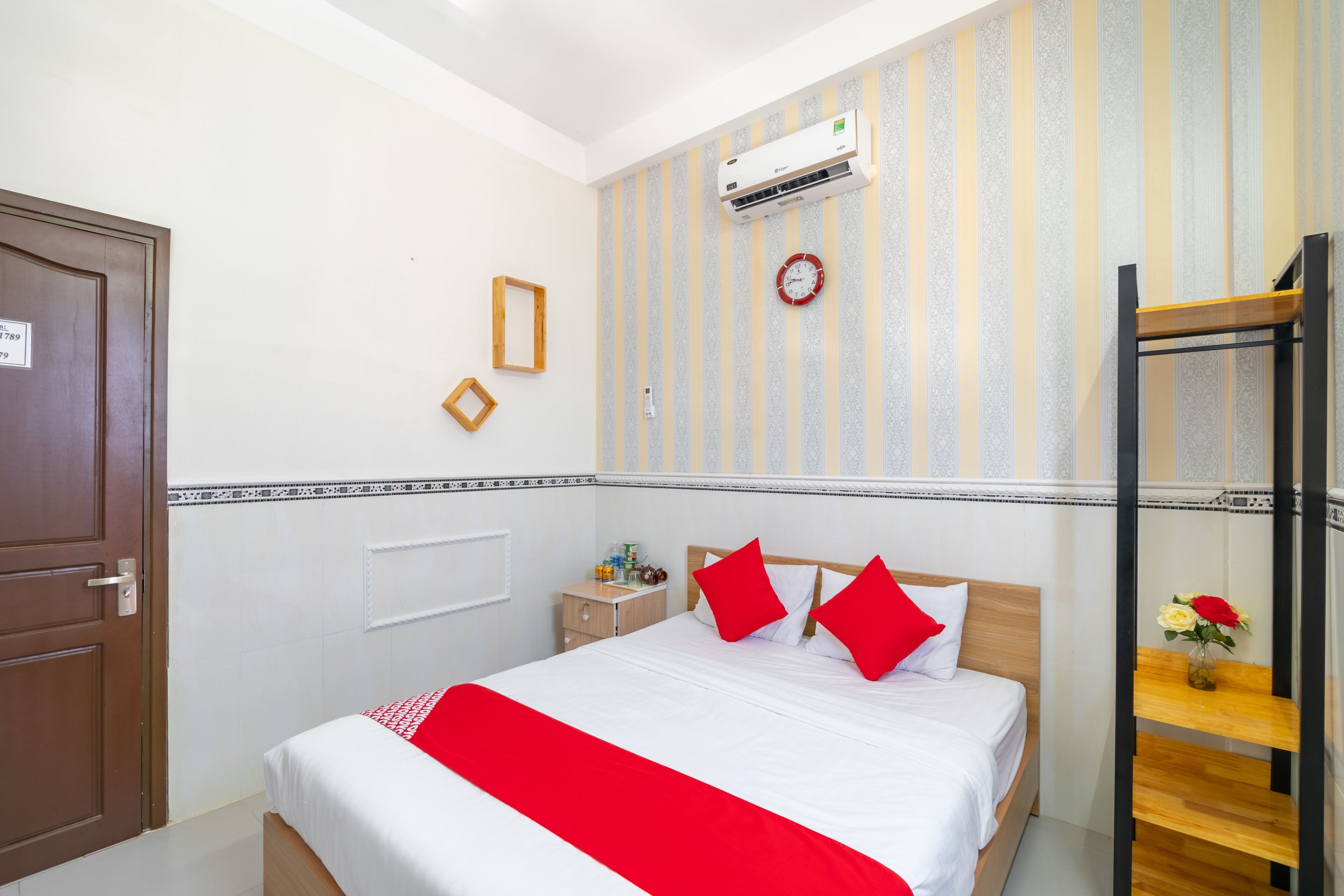 A hotel room with a bed, a nightstand, a wall clock, an air conditioning unit, and a bunk bed.