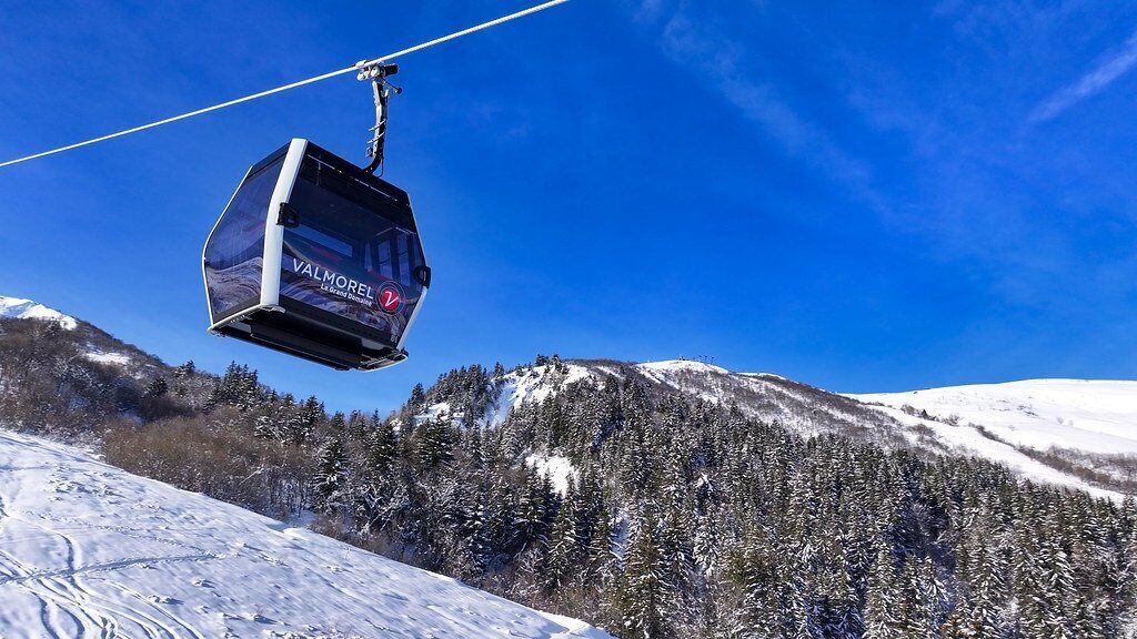 A cable car labeled "VALMOREL 2" suspended over a snowy mountain landscape with dense forests.