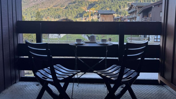 A balcony with two chairs and a table, overlooking a mountainous landscape with buildings in the background. - Bûche 13 - Cosy studio with movable partition (LES AVANCHERS VALMOREL)
