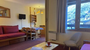 A cozy room with a sofa, a dining table, a chair, and a window with a view of a mountainous landscape. - Bûche 13 - Cosy studio with movable partition (LES AVANCHERS VALMOREL)