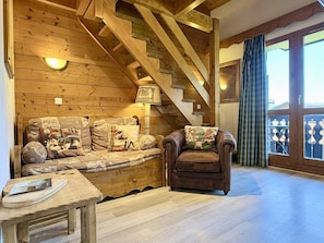 A cozy room with a wooden staircase, a sofa with patterned cushions, a leather armchair, and a wooden table.