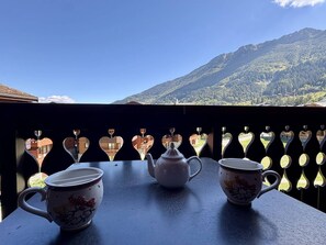 Ein Balkon mit einem für Tee gedeckten Tisch, mit Blick auf eine gebirgige Landschaft.