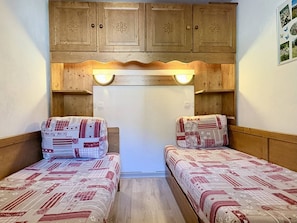 A small room with two beds, wooden cabinets above, and a wall-mounted light fixture.