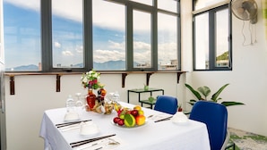A dining area with a table set for two, a vase of flowers, and a fruit bowl.