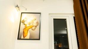 A framed artwork of a woman holding flowers on a wall, a window with a view of buildings, and a showerhead. - AHA Hoang Van Homestay Nha Trang (Bac Nha Trang)