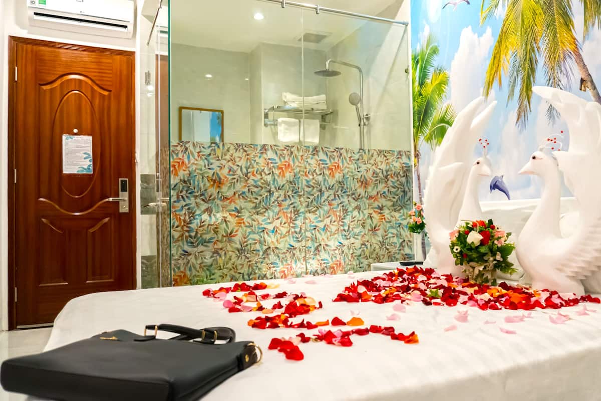 A hotel room with a bed, a wooden door, a shower, and a mural of swans and palm trees.