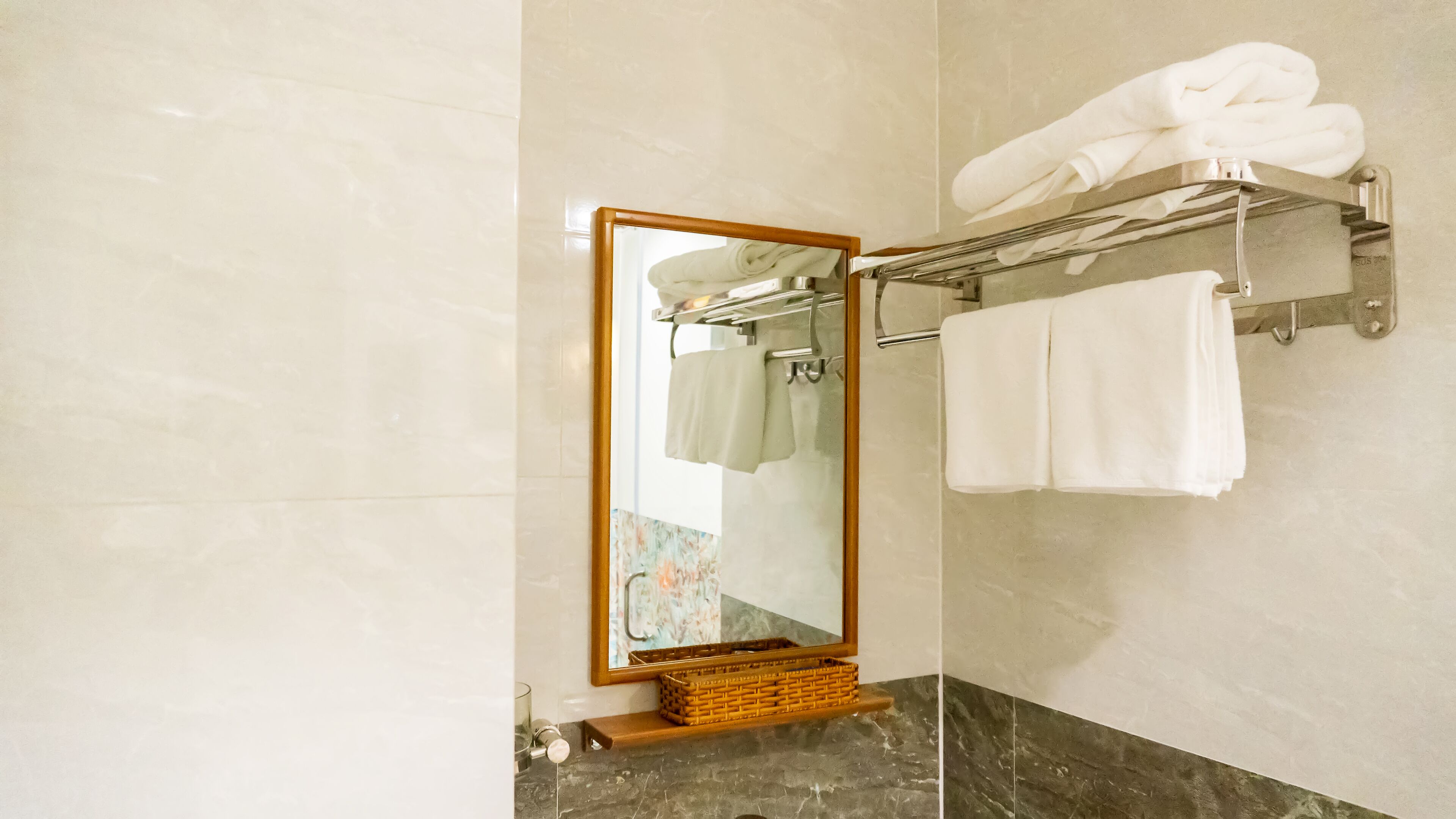 A bathroom with a large mirror, a towel rack with white towels, a wicker basket, and a marble countertop.