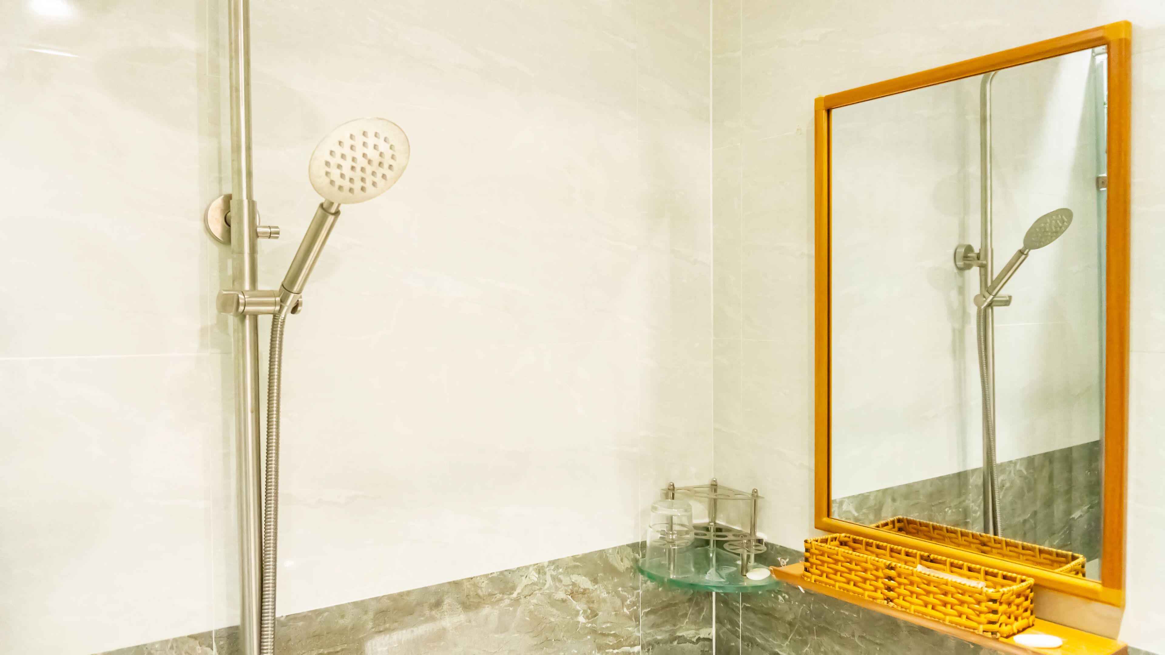 A bathroom with a shower, a glass shelf, and a mirror with a wooden frame.