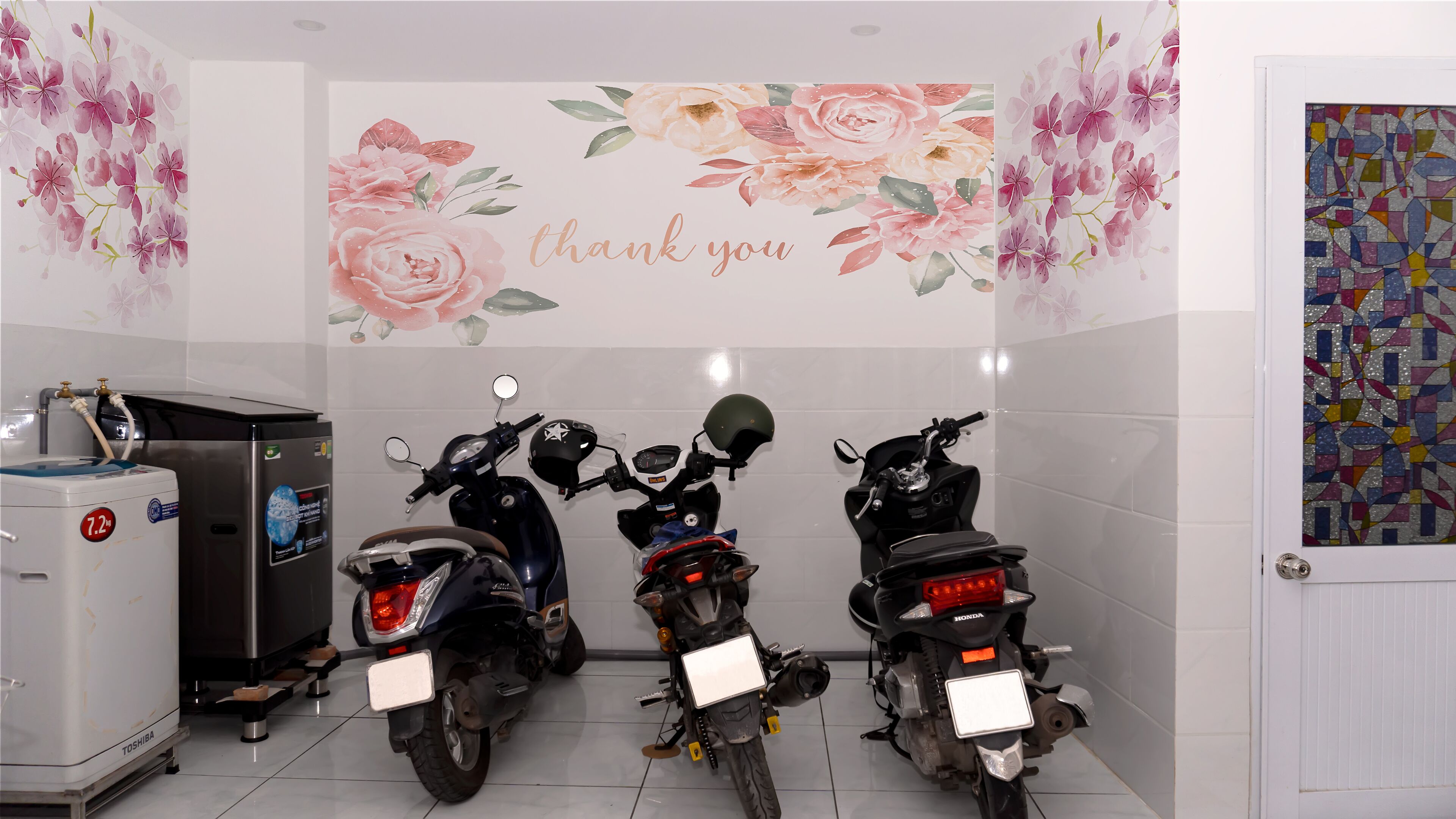 Un baño con tres motocicletas estacionadas en fila, un dispensador de agua y un revestimiento floral decorativo.