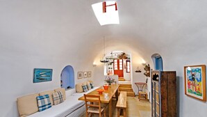 Une pièce chaleureuse et bien éclairée, avec une table à manger en bois, un banc, un canapé et un escalier menant à un niveau supérieur.