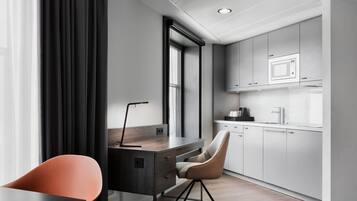Una cocina moderna con armarios blancos, un microondas y una cafetera. Hay un escritorio con una silla y una ventana con cortinas.