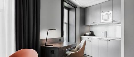 Una cocina moderna con armarios blancos, un microondas y una cafetera. Hay un escritorio con una silla y una ventana con cortinas.