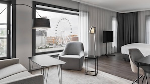 Una habitación de hotel moderna con un ventanal grande, una silla, una cama, un escritorio y una lámpara.