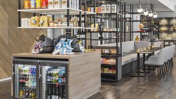 L’intérieur d’un restaurant moderne présente un comptoir en bois, un présentoir réfrigéré pour les boissons, des étagères remplies de collations et un espace détente avec des chaises.