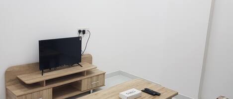A room with a wooden entertainment unit, a television, and a small table with a remote control and a tissue box.