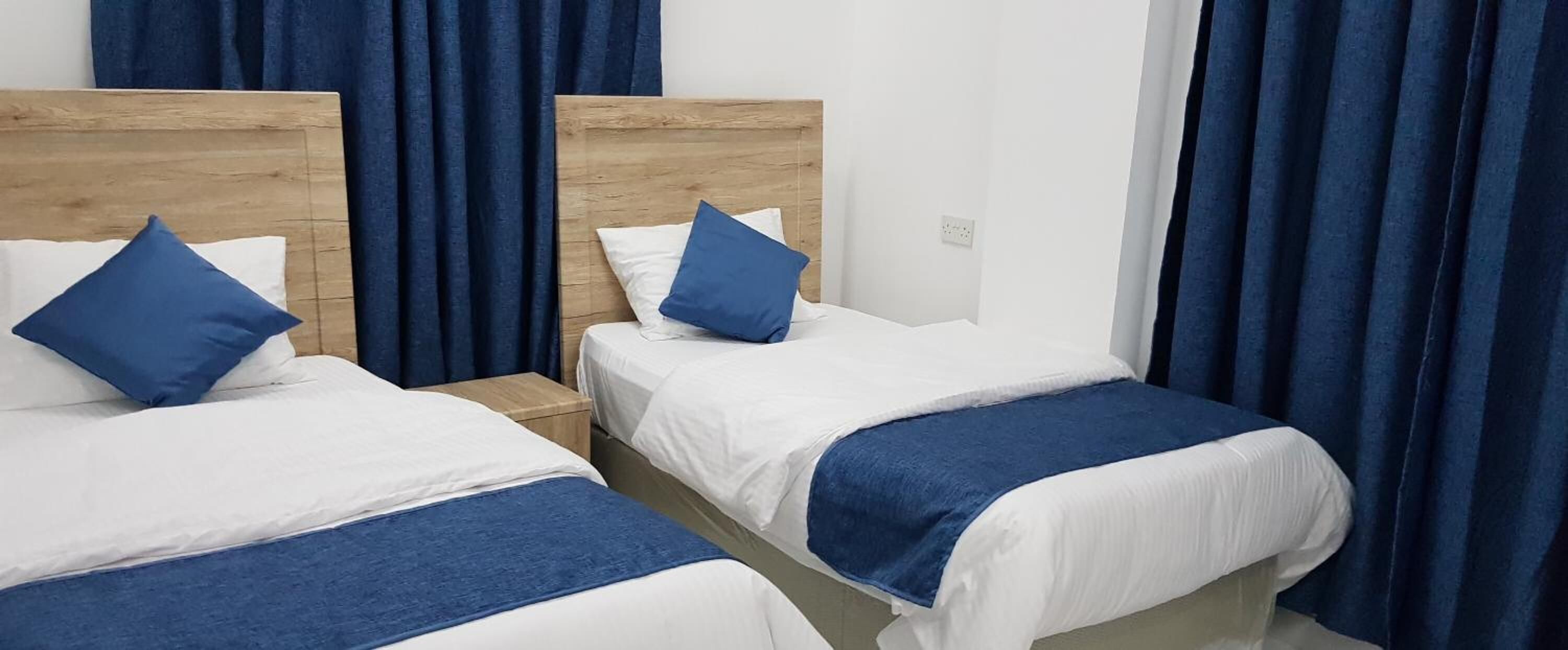 Dos camas individuales con cabeceros de madera, ropa de cama blanca y almohadas azules.