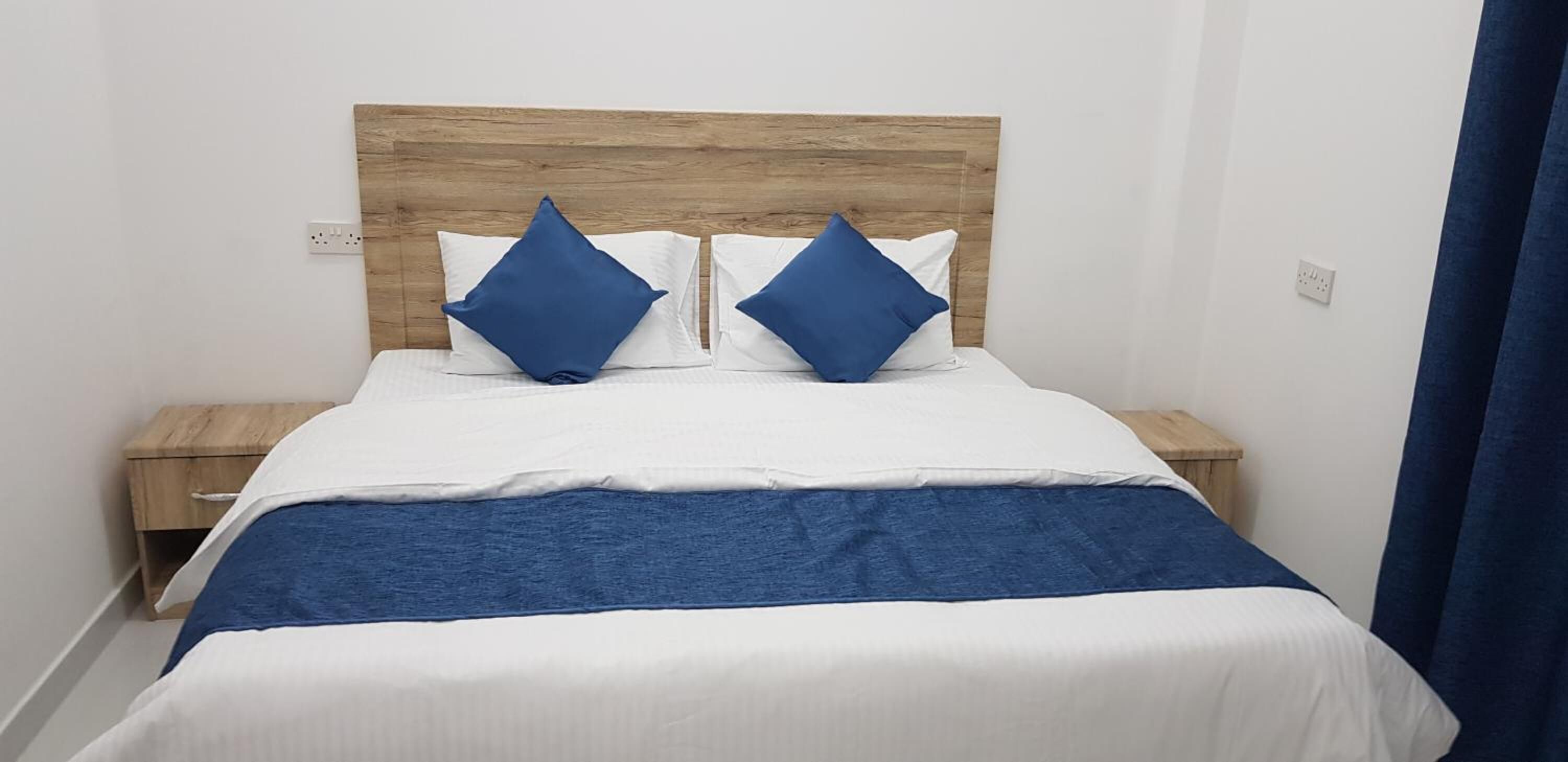 Una cama bien hecha con un cabecero de madera, dos almohadas y una colcha azul.