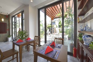 A dining area with tables set for two, large windows with a view of the outdoors, and a fire extinguisher on the wall.