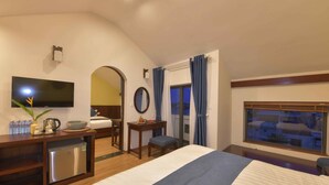 A hotel room with a bed, a desk with a refrigerator, a television, and a window with curtains. - Saclo Villa and Hostel (Da Nang)