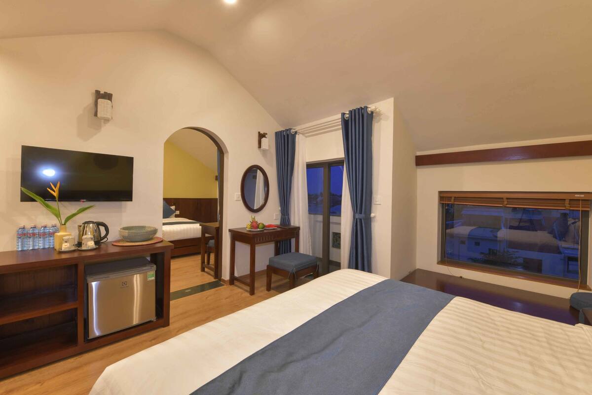 A hotel room with a bed, a desk with a refrigerator, a television, and a window with curtains.
