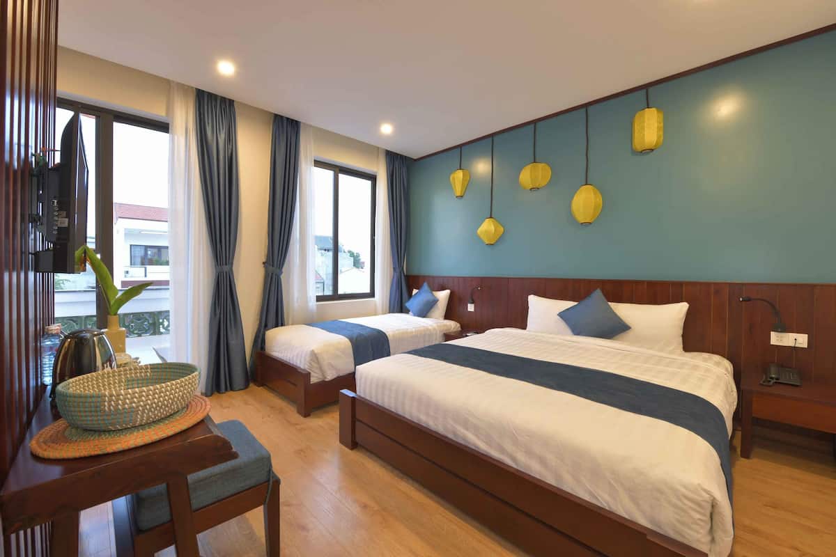 A hotel room with two beds, a wooden nightstand, a desk with a lamp, and a view of the outside.