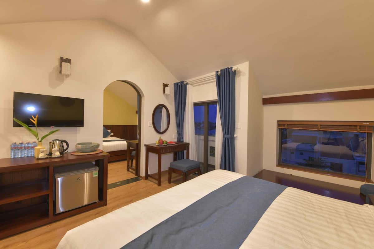 A hotel room with a bed, a desk with a refrigerator, a television, a window with curtains, and a view of the outside.