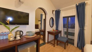 A hotel room with a TV, a dining table with a bowl and bottles, a small table with a plate and a cup, a bed, and a window with curtains. - Saclo Villa and Hostel (Da Nang)