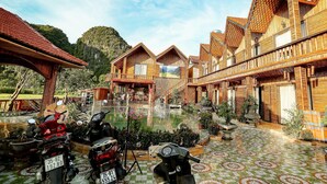 A traditional wooden building with a tiled courtyard, a covered seating area, and a view of a mountain. - Windy Fields Villa (Nam Hoa Lu)