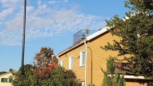 Een woongebouw met een bakstenen gevel, een balkon met een metalen hekwerk en een helderblauwe lucht.
