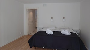 Een hotelkamer met een bed, twee nachtkastjes en een deur naar een andere kamer.