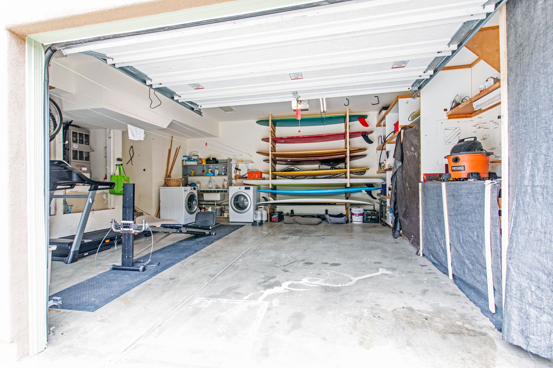 A garage with a washing machine, a treadmill, and a row of kayaks.