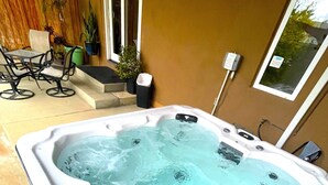 Ein Whirlpool mit einer gefliesten Terrasse, Gartenmöbeln und einem an der Wand montierten Heizgerät.