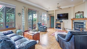 Ein großzügiges Wohnzimmer mit Ledersofas, einem Kamin, einem Fernseher und großen Fenstern mit Blick ins Freie.