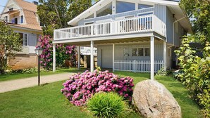 A two-story house with a balcony, surrounded by a well-maintained garden with pink flowers and a large rock.