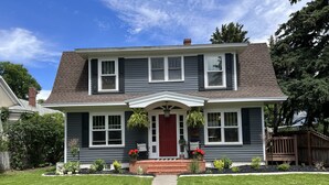 A two-story house with a red front door, white trim, and a front porch with hanging plants. - Cody's Downtown Den - DOWNTOWN - New listing & Pets Welcomed! (Cody)