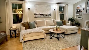 A living room with a beige sofa, a coffee table, and a patterned rug. There is a small side table with a lamp and a picture frame. - Cody's Downtown Den - DOWNTOWN - New listing & Pets Welcomed! (Cody)