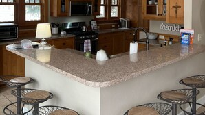 A kitchen with wooden cabinets, a granite countertop, and a central island with bar stools. - Cody's Downtown Den - DOWNTOWN - New listing & Pets Welcomed! (Cody)