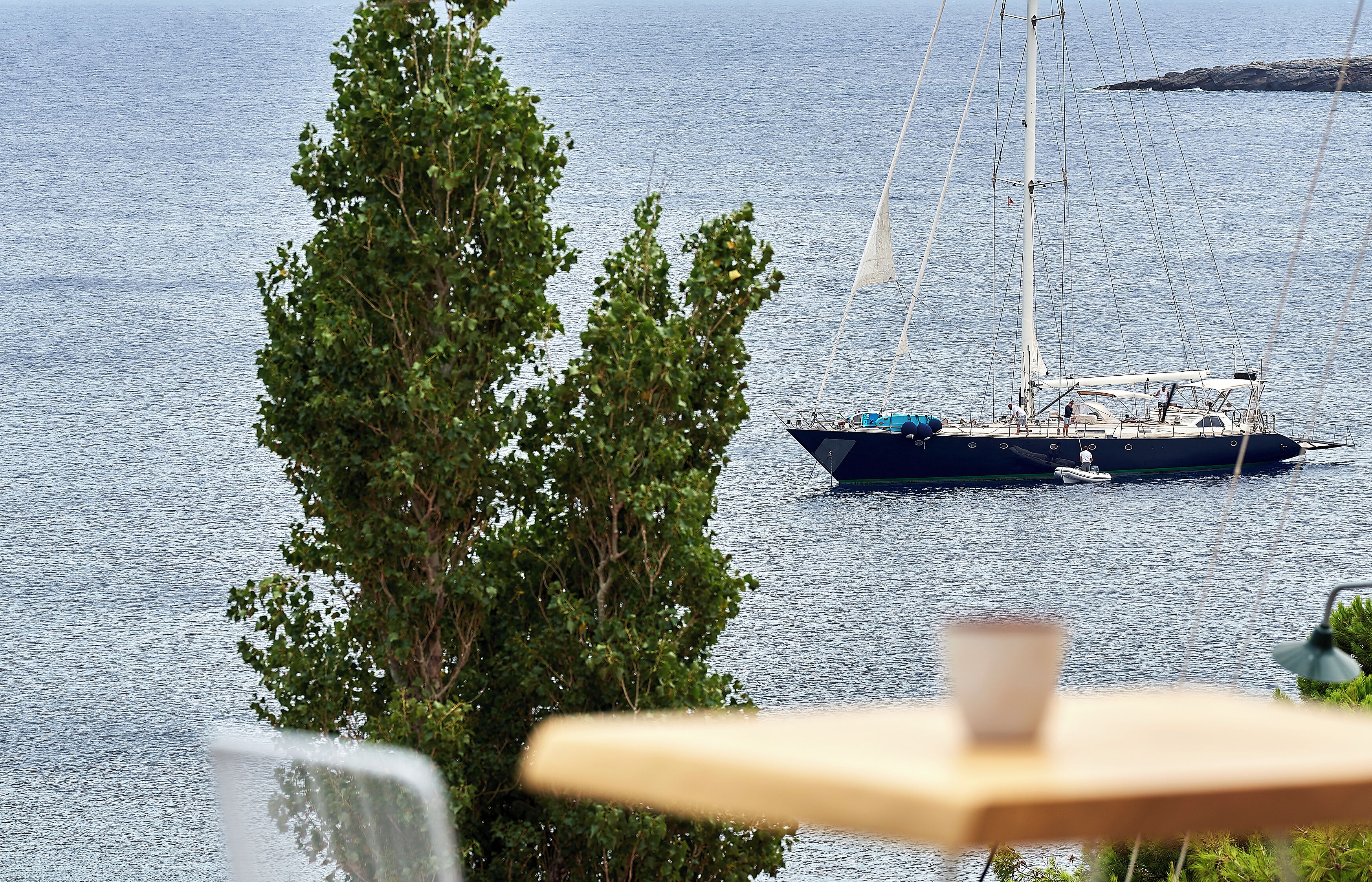 Una barca a vela su acque calme, un albero sullo sfondo e un tavolo con una tazza.
