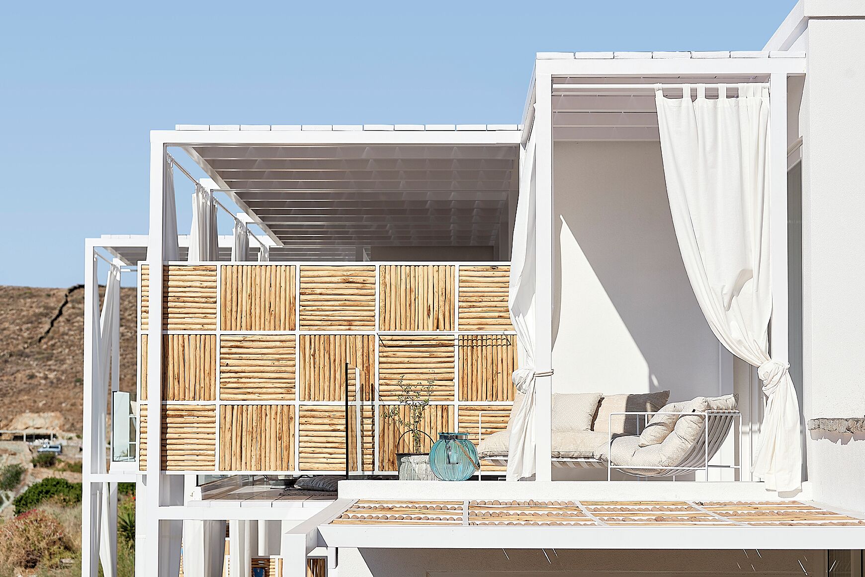 A modern building with a white exterior, a wooden panel wall, and a balcony with seating.