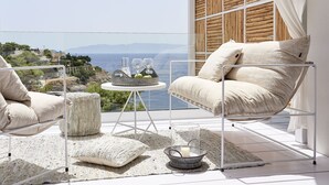 Un balcón con vista al mar, dos sillones acolchados, una mesita redonda con una vela y un cuenco de vidrio.
