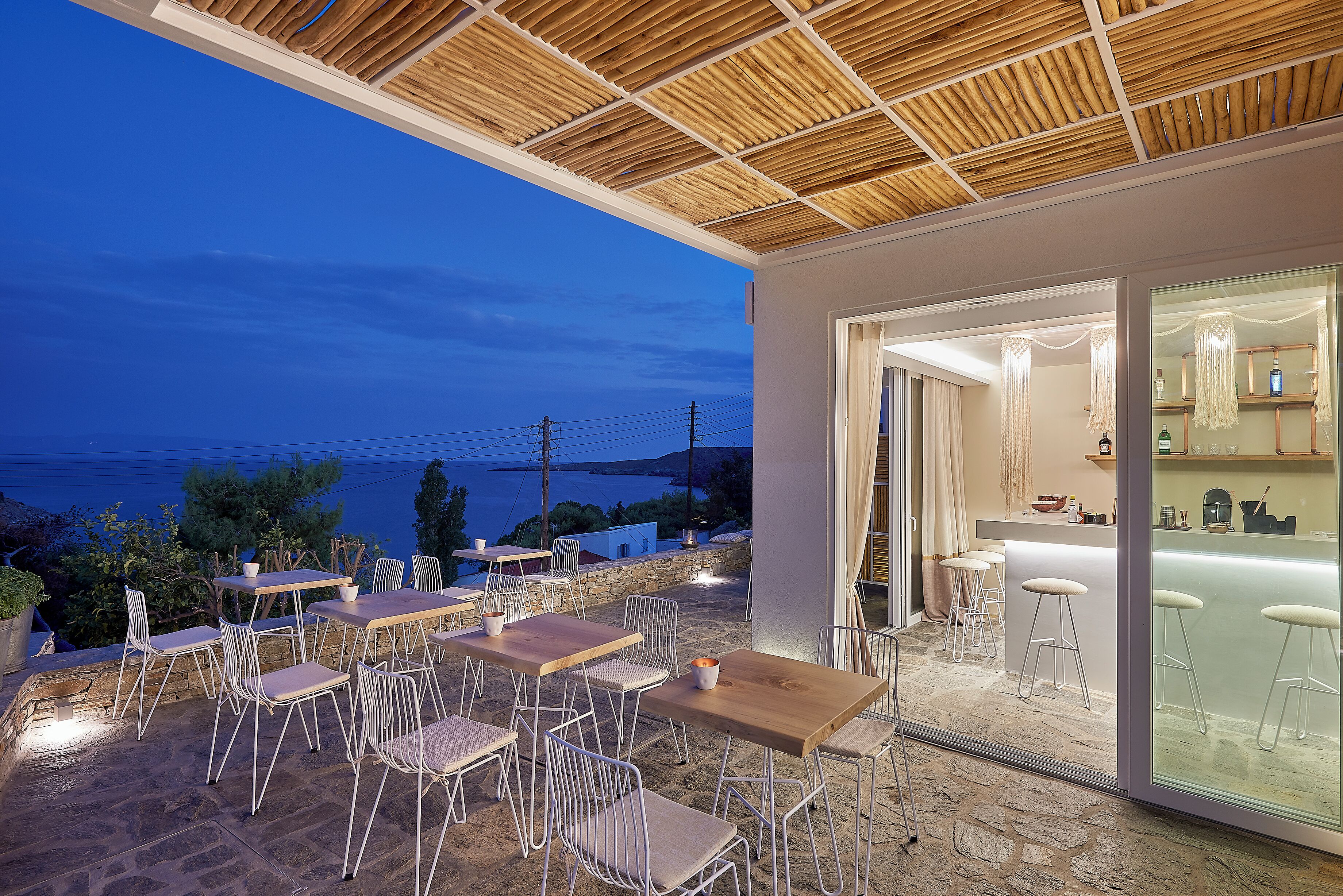 Zona pranzo all'aperto con tavoli e sedie, angolo bar con sgabelli e vista sul mare.
