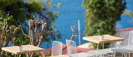 Outdoor seating with wooden tables and white chairs, overlooking a body of water.