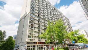 A tall, modern building with multiple floors, featuring a ground-level shop with a visible sign for 'OSTREHOJE'. - Comfortable Studio in the Center | Parking and Balcony (Warszawa)