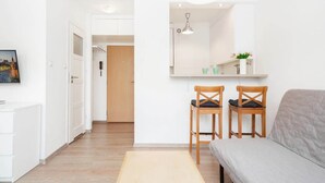 A modern, well-lit room with a sofa, two wooden chairs, a small table, and a mirror above the table. - Comfortable Studio in the Center | Parking and Balcony (Warszawa)