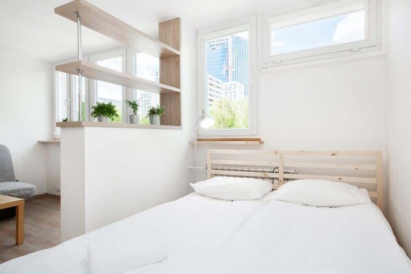A minimalist bedroom with a bed, bedside tables, a chair, and a window with a city view.