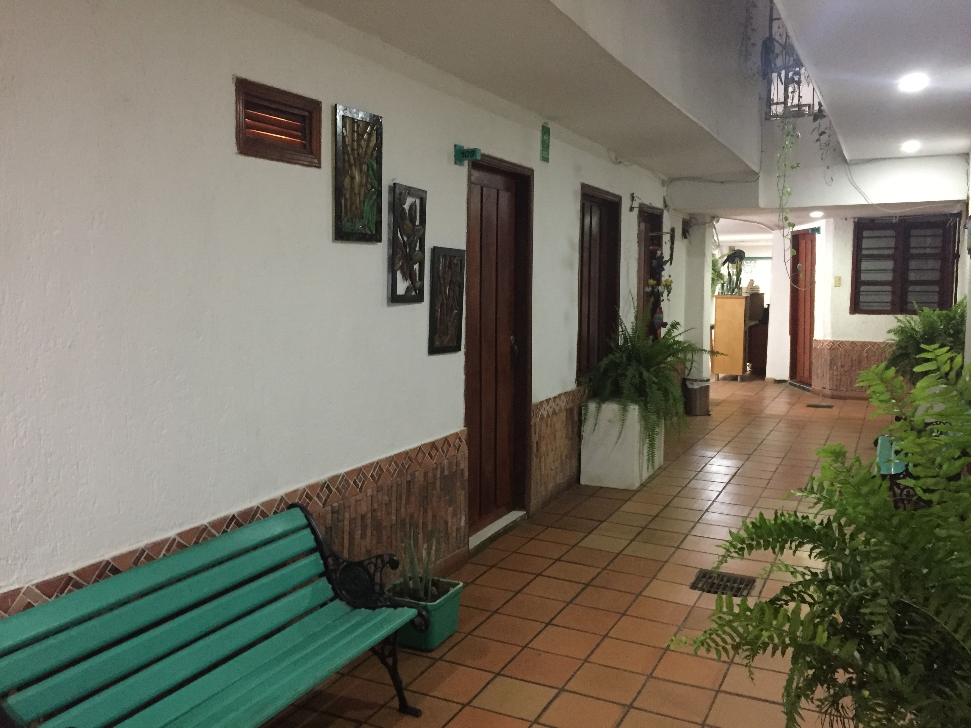 A corridor with a green bench, potted plants, and artwork on the walls.