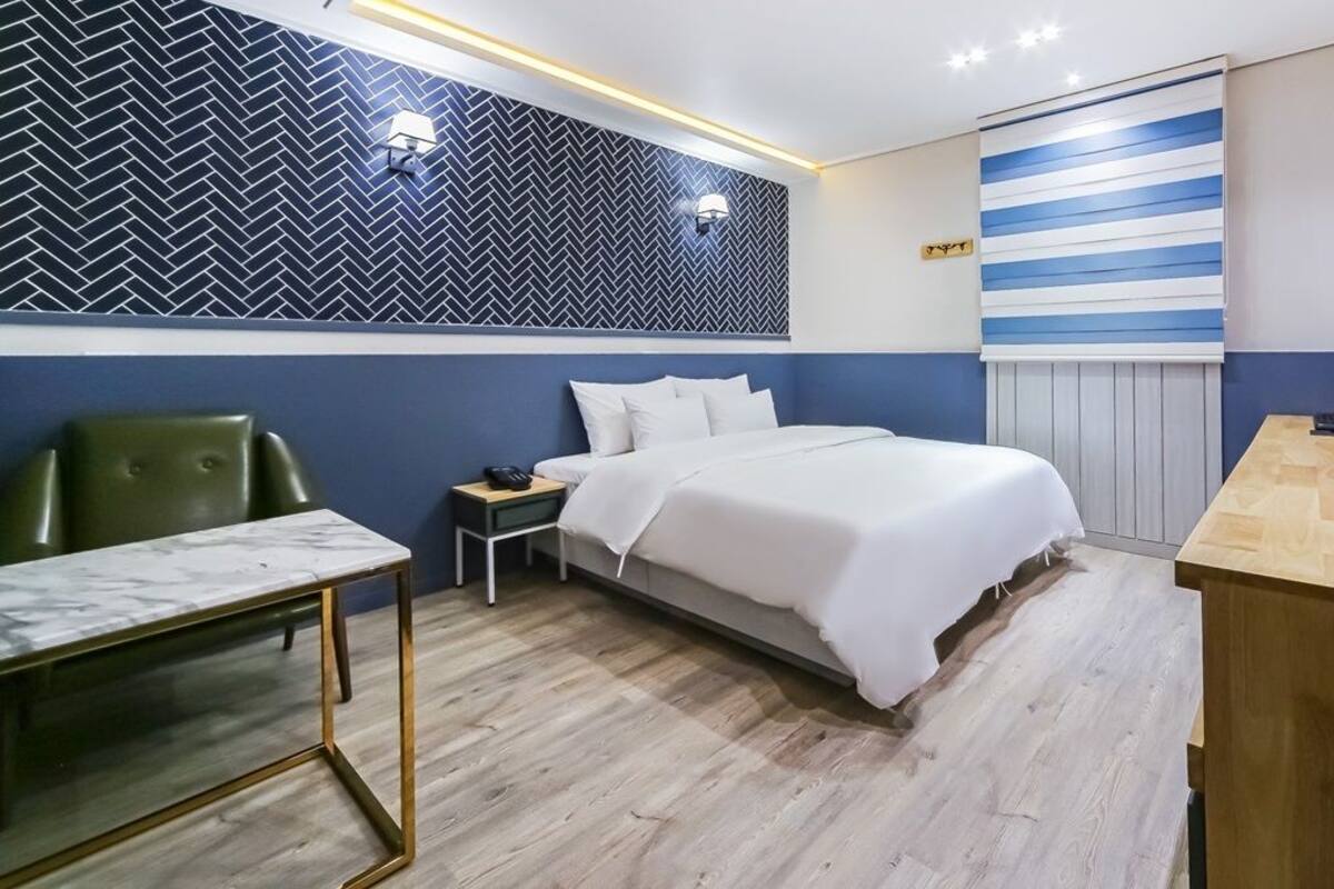 A modern hotel room with a bed, a desk, a chair, and a nightstand.